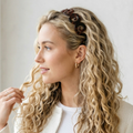 Woman with long, wavy blonde hair wearing a decorative headband against a white background