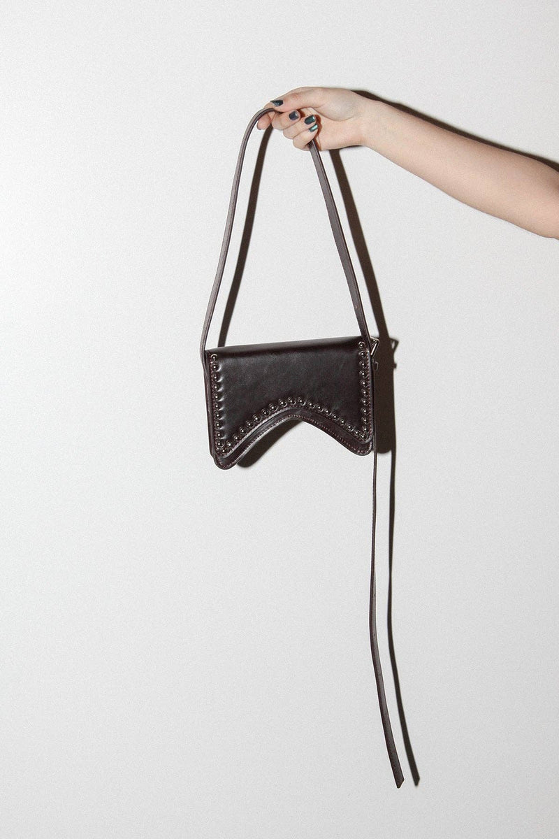Hand holding a black leather handbag with a strap against a white background