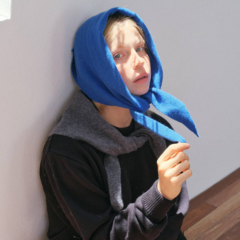 Person wearing a blue hood over their head against a light-colored wall.