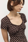 Woman wearing a brown polka dot dress against a plain background