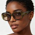 Woman wearing large, round sunglasses with a neutral background