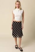 Woman wearing a white sleeveless top and black polka dot skirt on a beige background