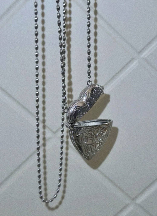 Silver necklace with a decorative pendant on a tiled wall background