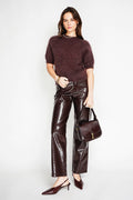 Woman wearing a maroon sweater and shiny brown pants holding a matching handbag on a white background