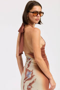 Woman wearing a brown halter top and patterned skirt with sunglasses on a white background