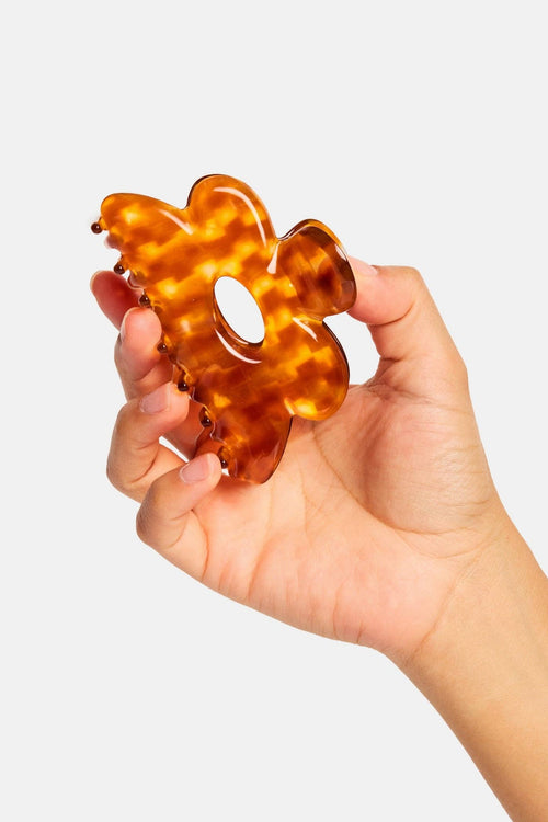 Hand holding a tortoiseshell patterned hair tie against a light gray background
