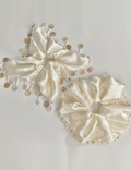 Two cream-colored satin hair bows with gold beads on a light gray background