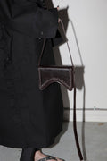 Person holding a dark brown leather bag with a plain background