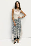 Woman wearing a white lace top and gray floral skirt against a white background