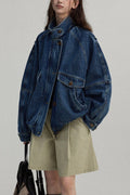 Person wearing a blue denim jacket and beige shorts against a plain background