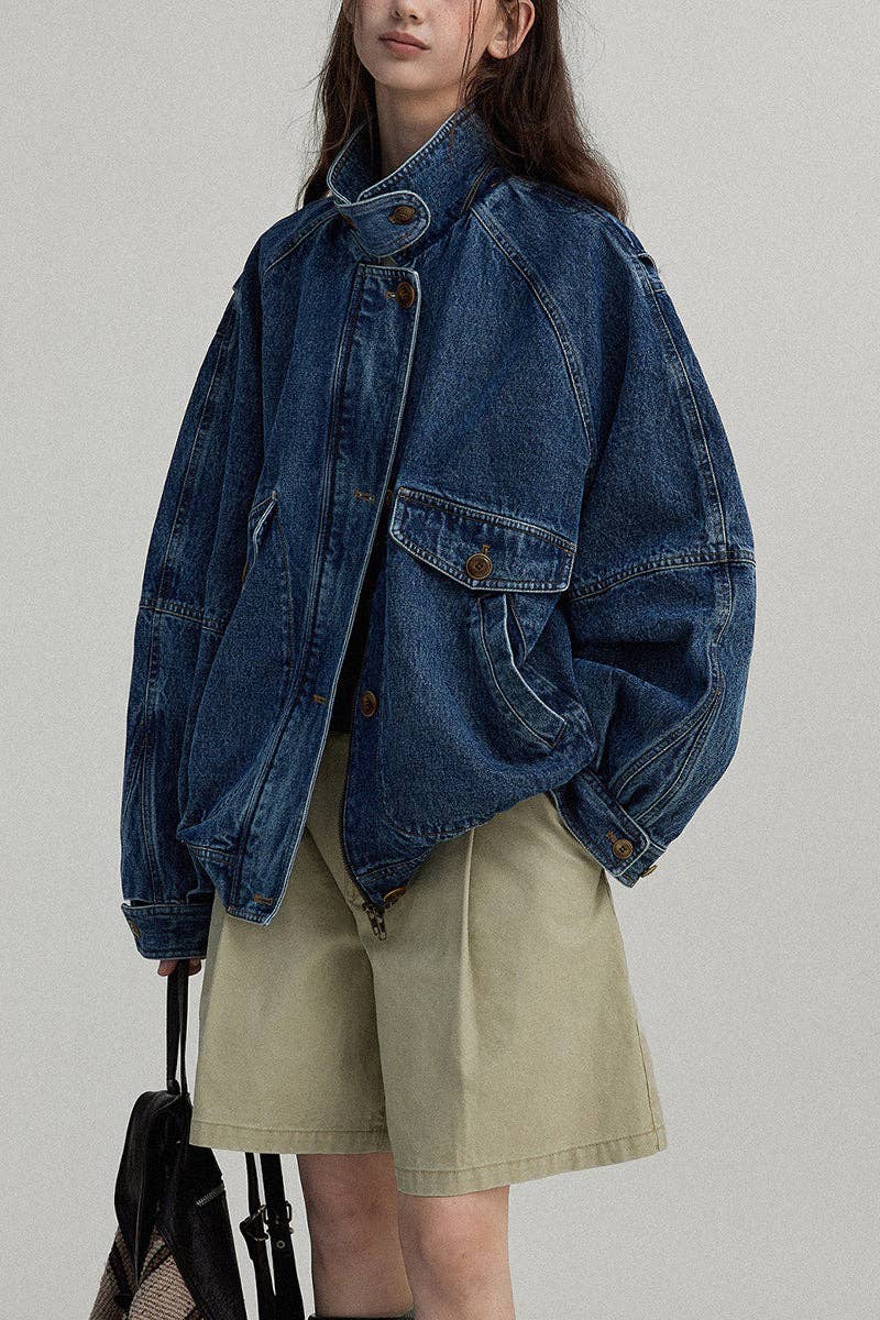 Person wearing a blue denim jacket and beige shorts against a plain background