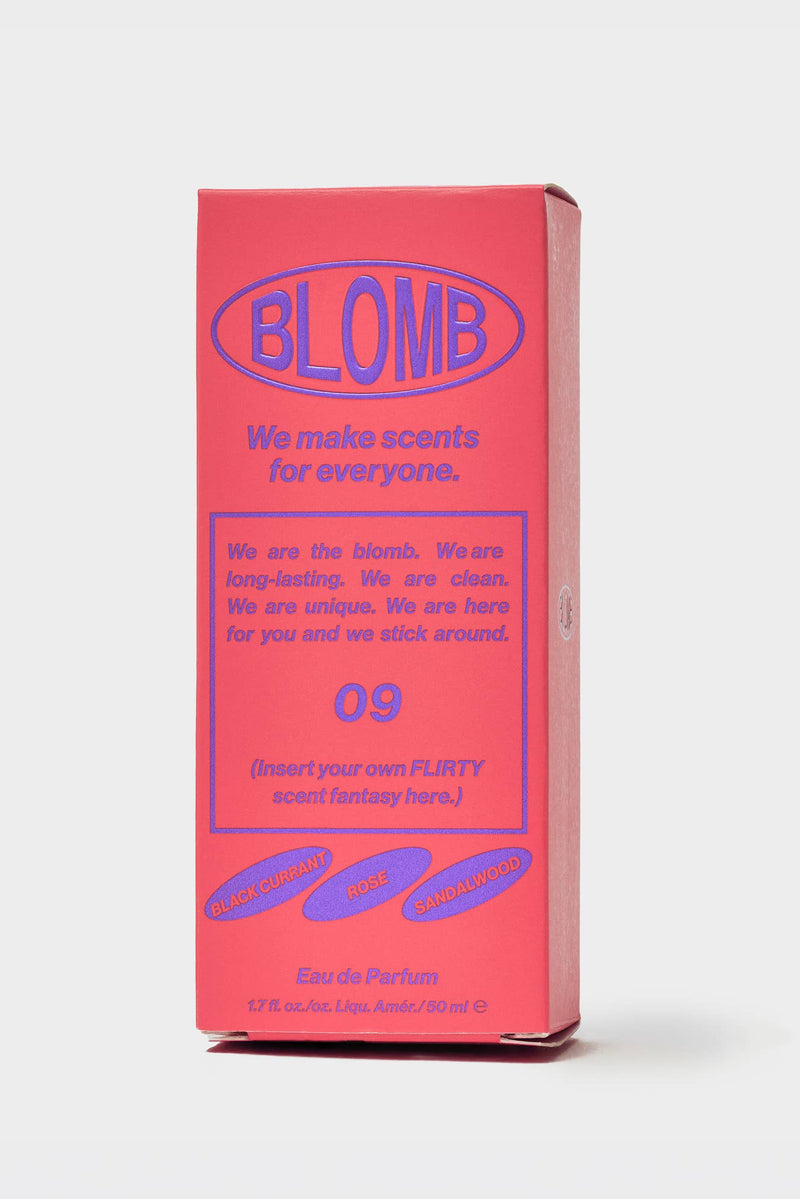 A tall rectangular pink product box with blue text and graphics, standing upright on a light gray studio background. The box prominently reads BLOMB and appears to be the packaging for a scent product.