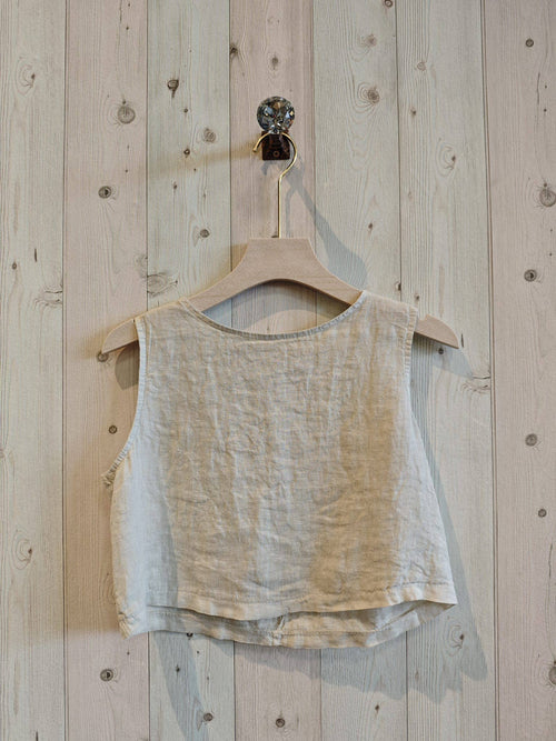 Beige tank top on a wooden hanger against a wooden wall.