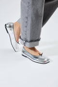 A person wearing silver tabi flats with a split-toe design, paired with gray jeans.