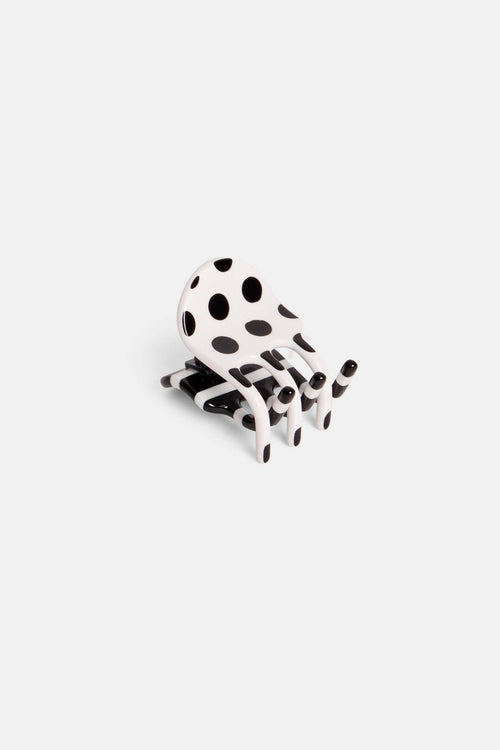 A small black and white polka dot accessory with a curved, chair-like silhouette, photographed on a plain light gray background.