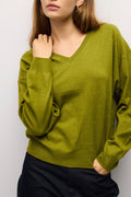 A woman wearing a long-sleeve olive green V-neck knit sweater and dark navy pants, shown from the chin down against a light gray background.