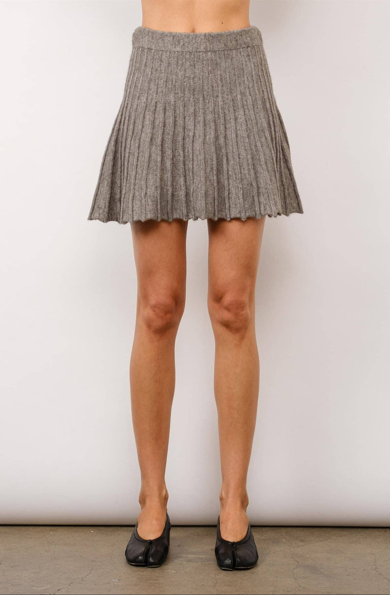 Person wearing a gray pleated skirt with black shoes on a plain background