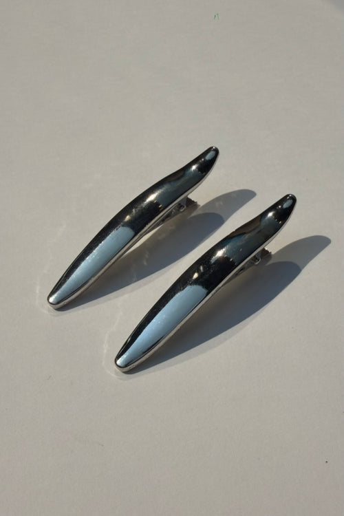 Two metallic silver hair claw clips with a glossy finish, displayed on a light gray surface with soft shadows.