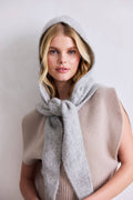 Woman wearing a gray hooded scarf and beige vest against a plain background