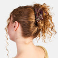 Person with curly hair tied back with a decorative scrunchie on a white background