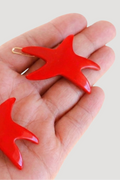 Red starfish-shaped earrings held in a hand with 'French Annie' branding.