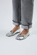 Silver metallic shoes worn with rolled-up gray jeans on a white background.