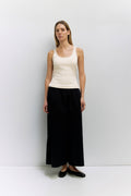 Woman wearing a white tank top and black skirt against a white background