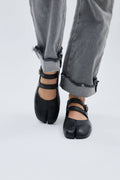 Black open-toe shoes worn with gray jeans on a light gray background