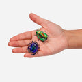 Two realistic beetle-shaped body jewelry pieces displayed on a person's open palm against a plain light gray background.