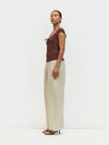 Woman wearing a brown top and beige pants against a white background