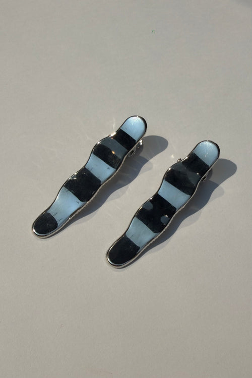 Two wavy hair clips with alternating black and light blue enamel stripes and silver metal borders, displayed on a neutral gray background.