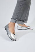 Silver metallic shoes worn with gray jeans on a neutral background