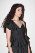 Woman wearing a black peplum top with ruffles against a white background