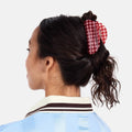 Person wearing a traditional outfit with a red and white checkered hair accessory on a white background