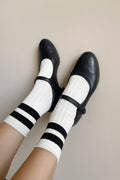 Black shoes with white socks featuring black stripes on a neutral background
