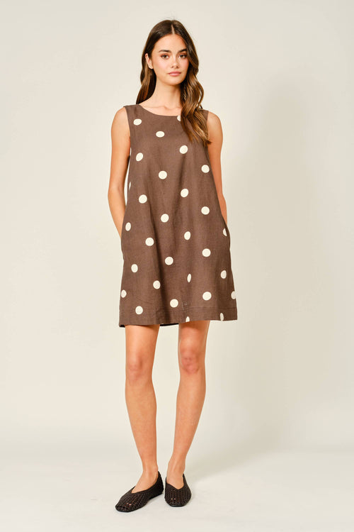 Woman wearing a brown dress with white polka dots on a plain background