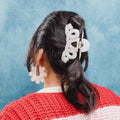 Person with a ponytail wearing a white hair clip and earrings against a blue background