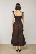 Woman wearing a brown dress with ruffled straps against a plain background