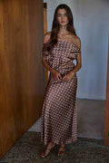 Woman wearing a brown polka dot dress standing in a room with wooden walls.