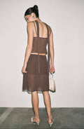 Woman wearing a brown dress with sheer panels against a plain background