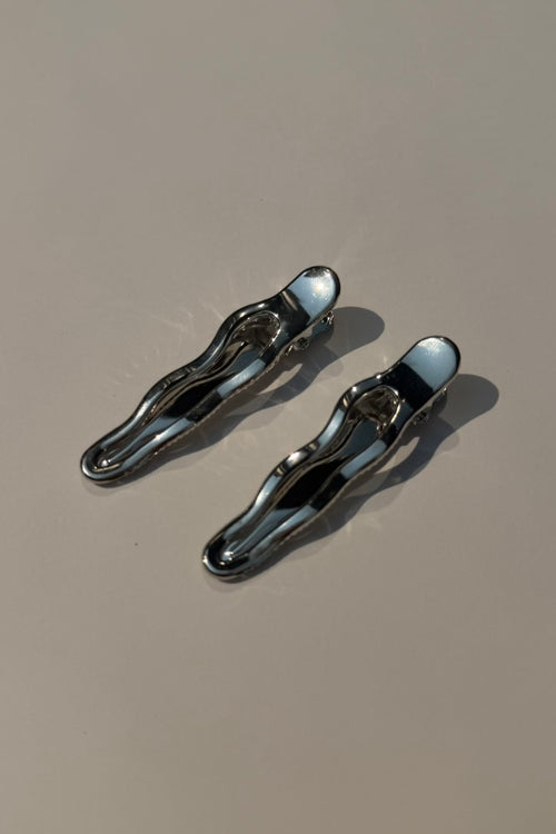 Two metallic silver hair claw clips on a plain beige surface with soft shadows.