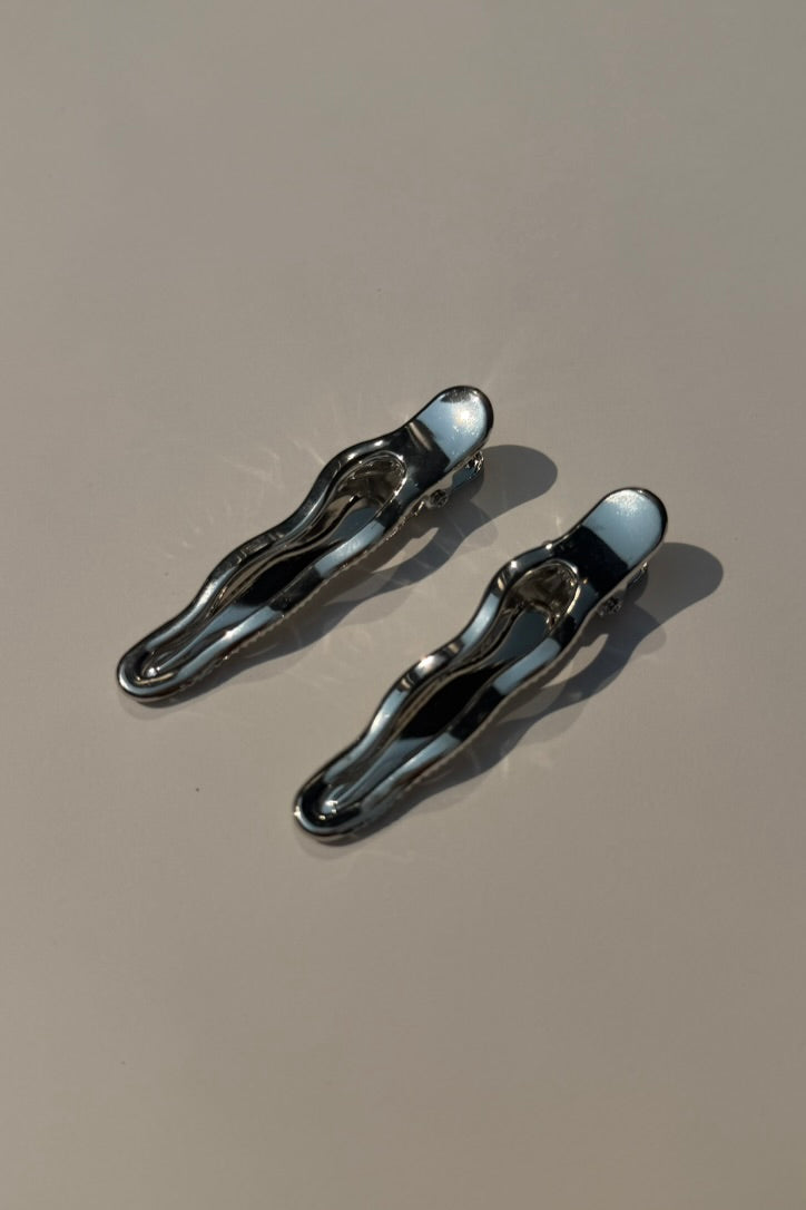 Two metallic silver hair claw clips on a plain beige surface with soft shadows.