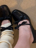 Black shoes with bows worn with white socks on a textured surface