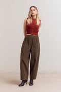Woman wearing a red sleeveless top and brown high-waisted pants against a plain background