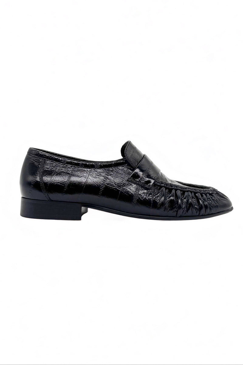 A single black leather moccasin-style loafer with a crocodile-embossed texture and a low block heel, shown in profile against a plain white background.