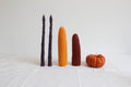 Set of four uniquely shaped candles on a white tiled surface with a small pumpkin.