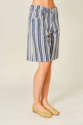 A person wearing knee-length vertical striped shorts in navy blue and white, paired with beige woven flat shoes, photographed against a plain light beige studio background.