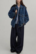 Person wearing a denim jacket and dark pants on a plain background