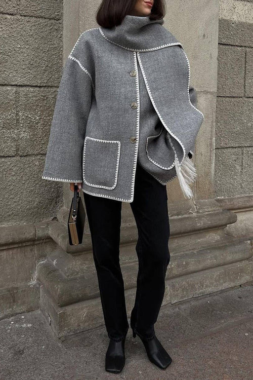 Person wearing a gray coat with white trim against a stone wall.