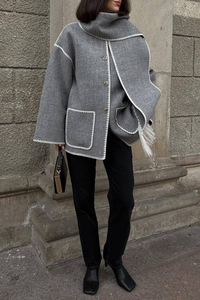 Person wearing a gray coat with white trim against a stone wall.